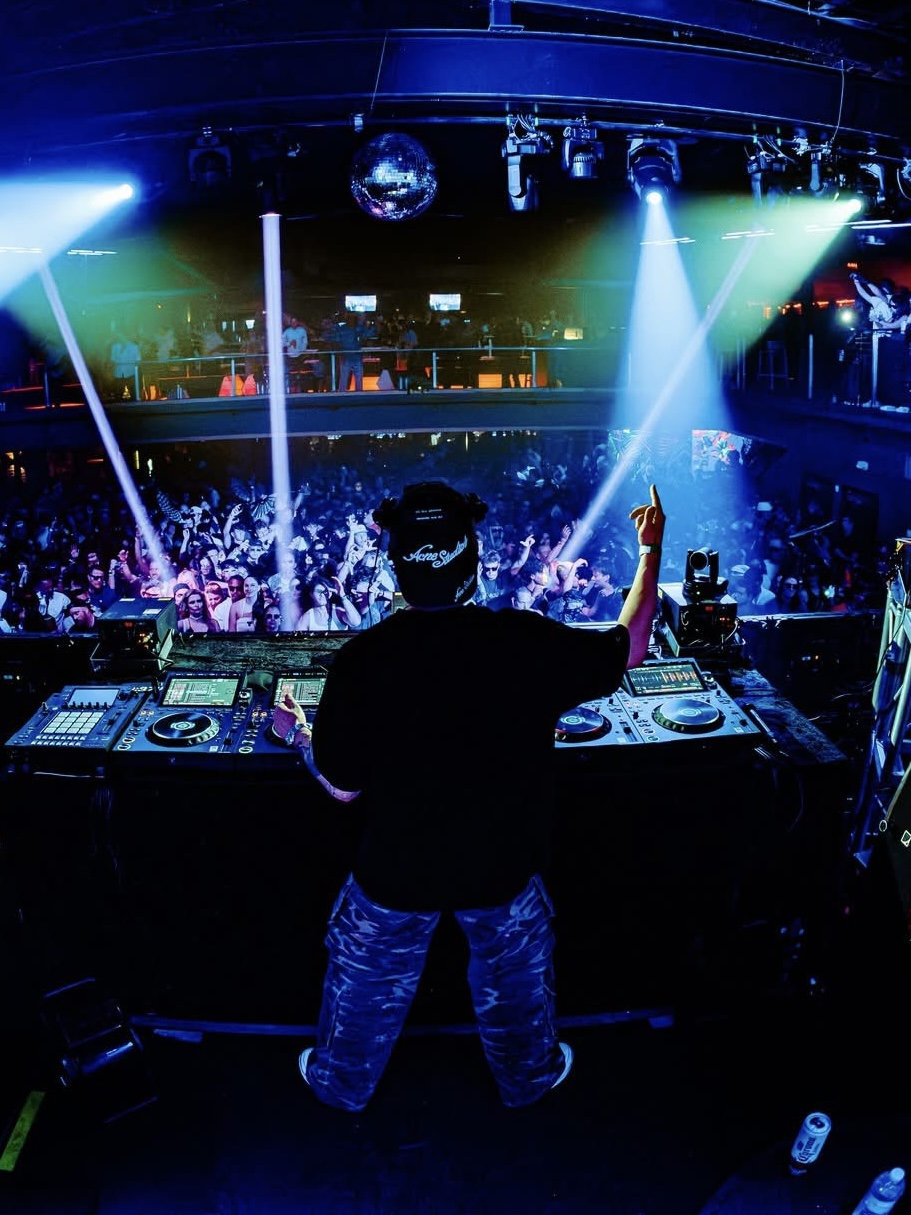 SUBSHIFT behind the decks, facing a packed crowd under blue and green club lights